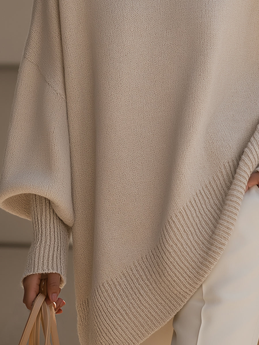 Woman wearing an oversized poncho sweater with asymmetric ribbed hem and mock neck