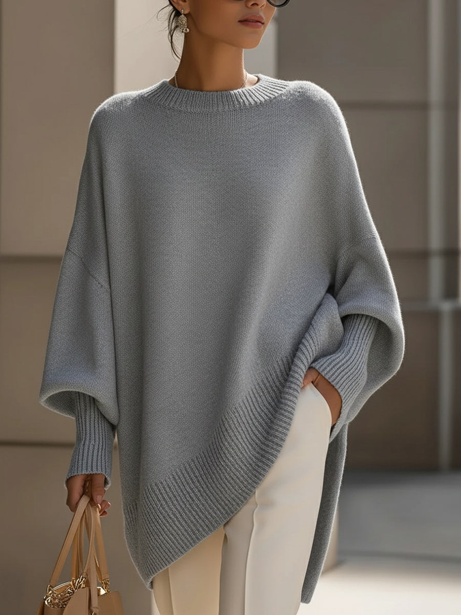 Woman wearing an oversized poncho sweater with asymmetric ribbed hem and mock neck
